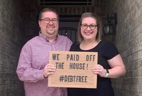 Photo of Rachel and Scott holding a letter board that says "We paid off the house! #debtfree"