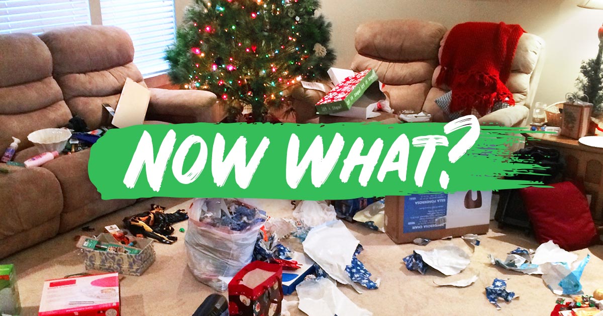 A living room decorated for Christmas is covered in torn wrapping paper and discarded ribbons. 