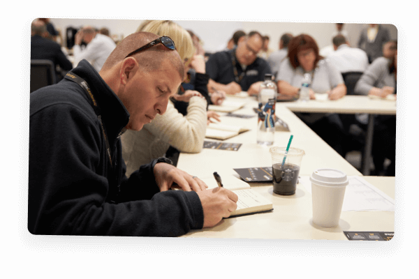 Man seated at a table, writing in a journal at a workshop.