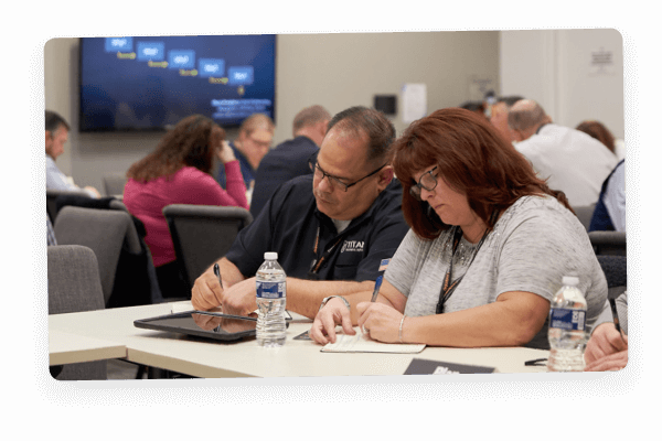 Man and woman seated at a table, writing notes for a workshop.