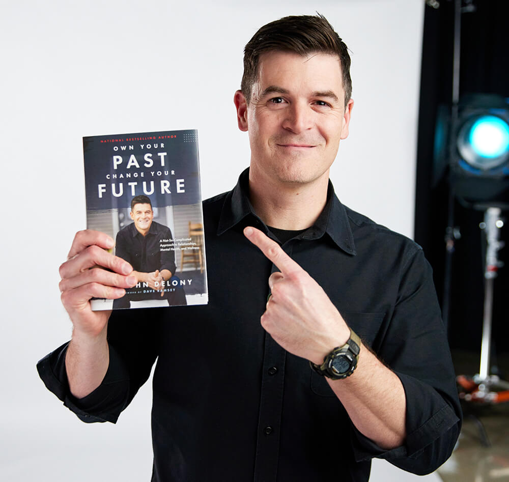 Photo of John holding his book "Own Your Past, Change Your Future"