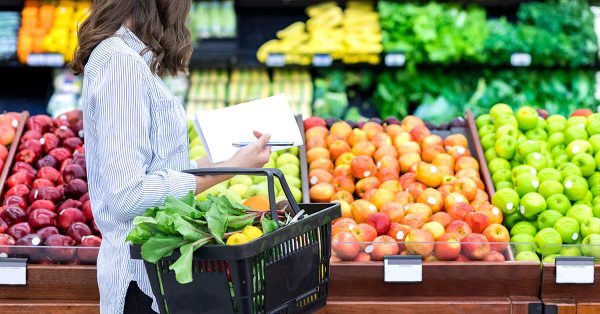A woman evaluating produce in the produce aisle of a grocery store.
