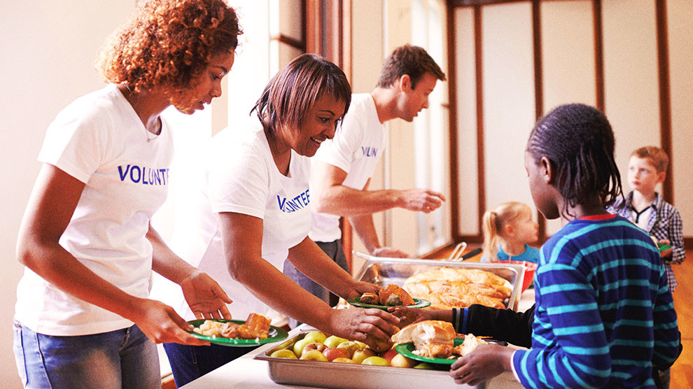 Three people with volunteer shirts standing in a line put together plates of food for children